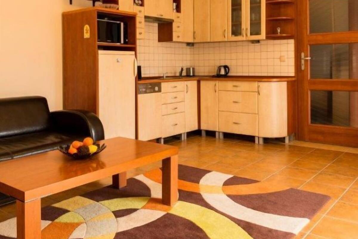 Une cuisine compacte avec des meubles en bois, un four à micro-ondes et un évier. On y trouve une table à manger avec un panier de fruits et un tapis à motifs.