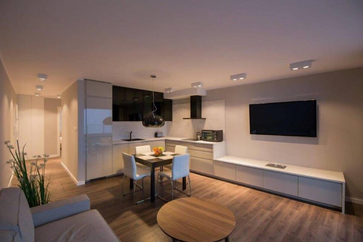 Une cuisine moderne avec des meubles blancs, un coin repas comprenant une table et des chaises en bois, un banc intégré et un téléviseur à écran plat fixé au mur.