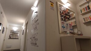 A hallway with a mirror, a wall with multilingual welcome messages, and a bookshelf with books. - DiMoras House (Verona)