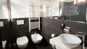 A modern bathroom with a white toilet, bidet, and a large white sink with a mirror above it. - DiMoras House (Verona)