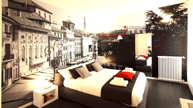 A modern bedroom with a cityscape mural, a large bed, and a view of a city skyline. - DiMoras House (Verona)