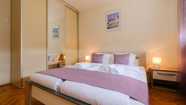 A neatly made bed with a pink blanket, a bedside table with a lamp, and a wall-mounted picture. - 3rooms downtown Belgrade (Belgrade)