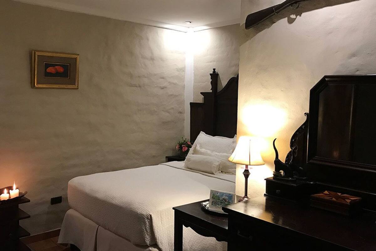 A bedroom with a bed, bedside table, lamp, and a framed picture on the wall.