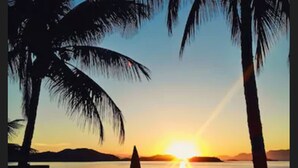 A sunset view from a deck with palm trees, a railing, and a table with chairs. - Pousada das Flores (Angra dos Reis)