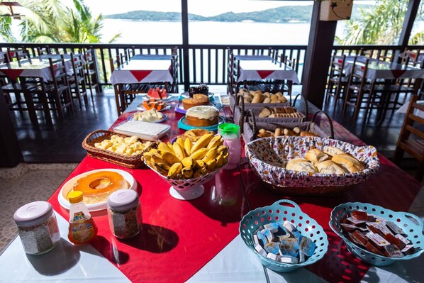 A buffet table with various food items and condiments, set against a backdrop of a scenic view. - Pousada das Flores (Angra dos Reis)