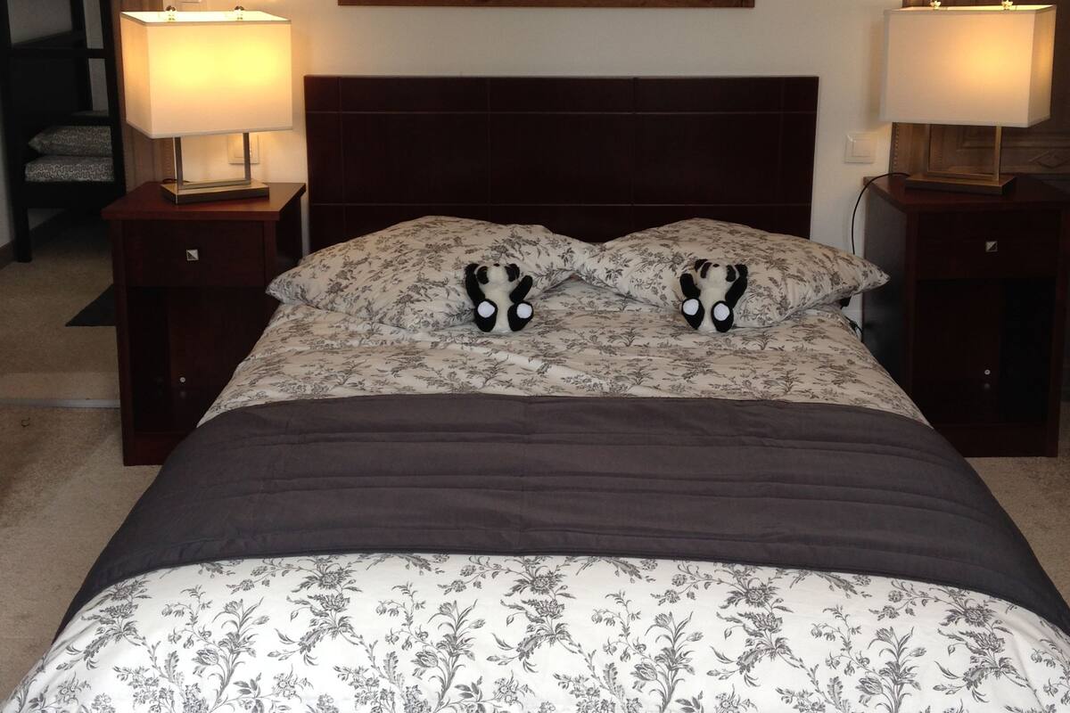 A bedroom with a large bed, two bedside lamps, a painting above the bed, and a nightstand with a lamp.