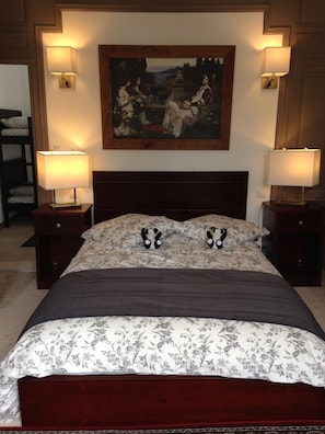 A bedroom with a large bed, two bedside lamps, a painting above the bed, and a nightstand with a lamp. - Maison du chatelain (Saint-Aignan)