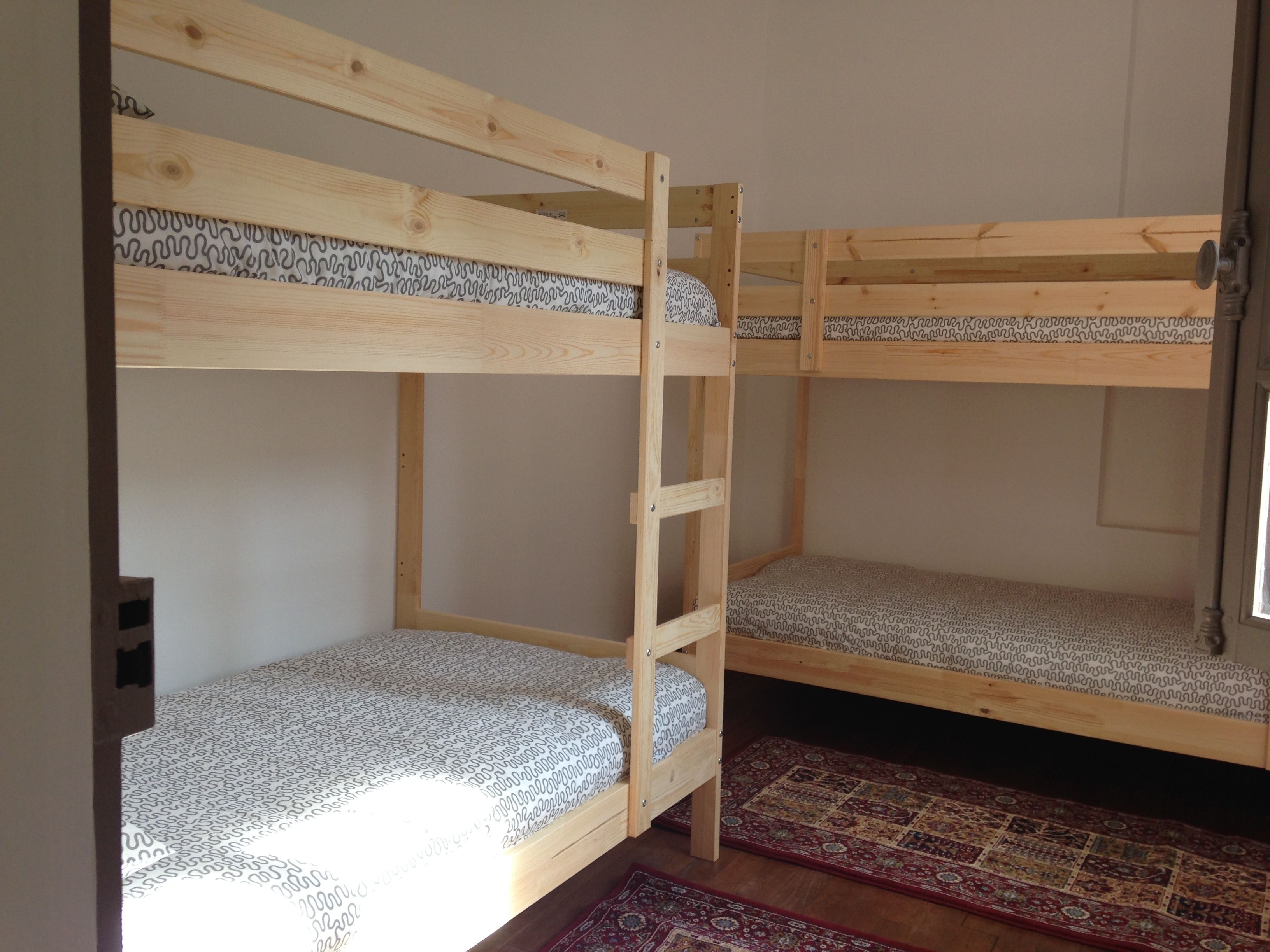 Habitación con literas, una escalera de madera, un colchón estampado y una alfombra roja en el suelo.