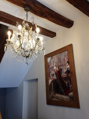 A room with a chandelier, wooden beams, and a framed historical painting. - Maison du chatelain (Saint-Aignan)