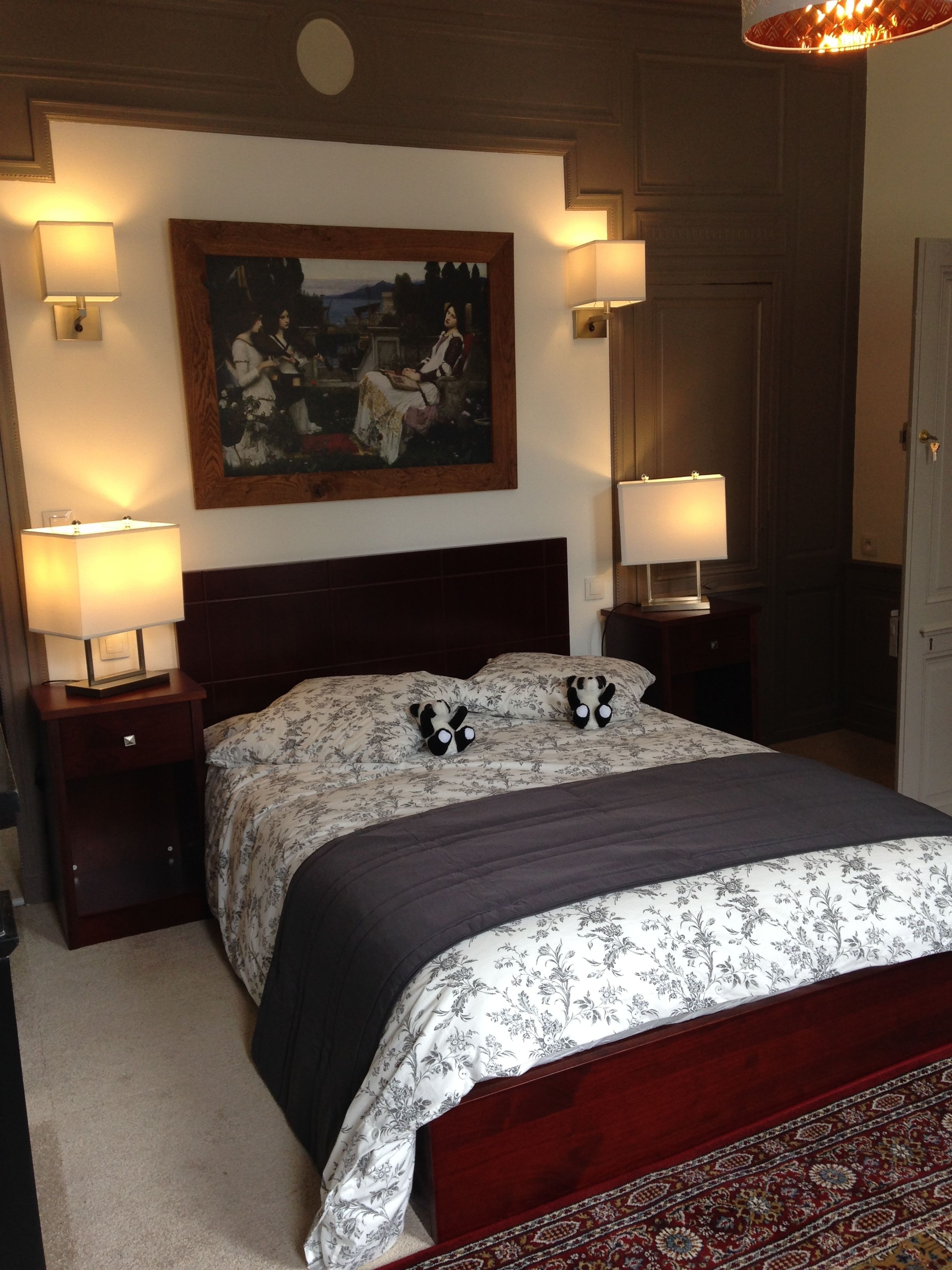 A bedroom with a large bed, two bedside lamps, a painting on the wall, and a patterned rug.