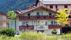 Un edificio de dos pisos con balcones, piscina y montañas al fondo.