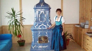 Una persona de pie junto a una estufa azul con diseños decorativos, en una habitación con paneles de madera y un sofá azul.
