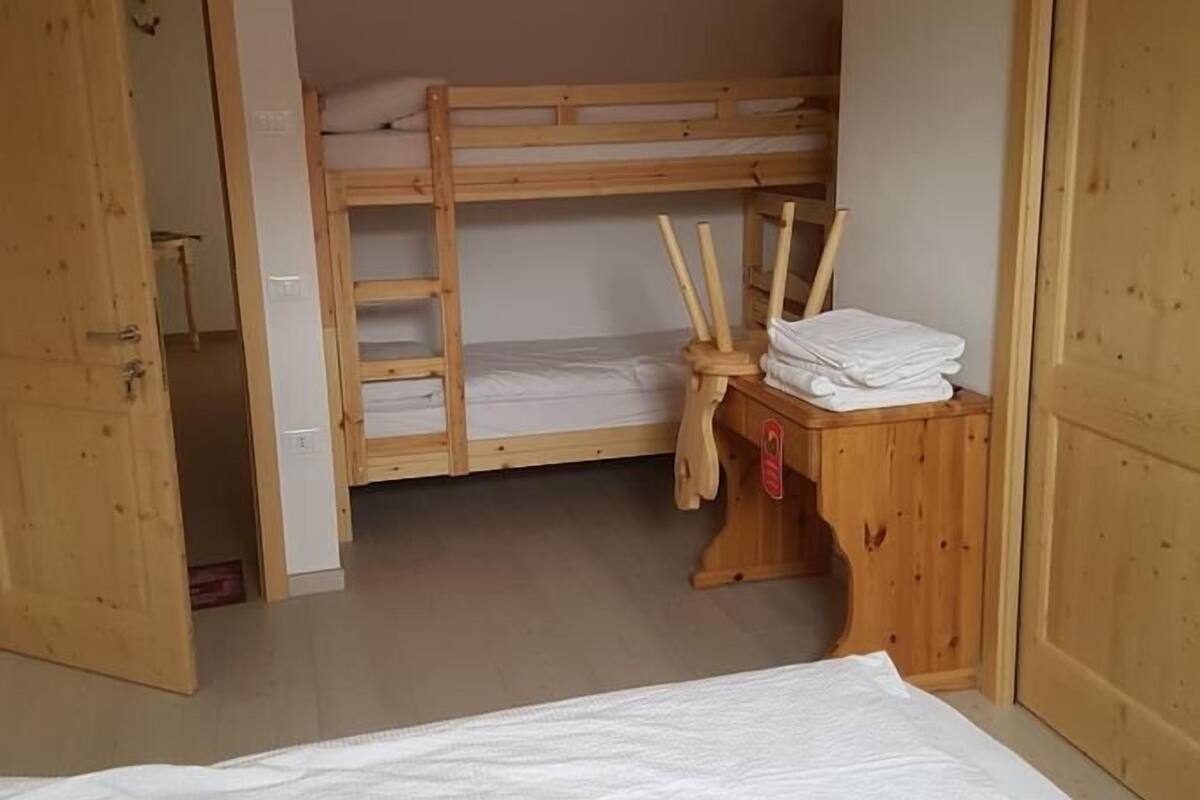 Ett rum med en våningssäng, ett skrivbord i trä med en stol och en garderob.