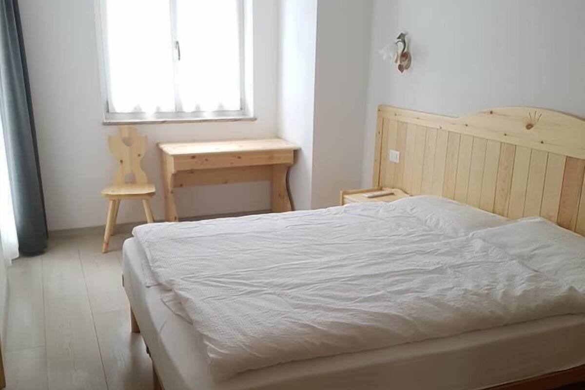 Ett sovrum med en säng och ett skrivbord i trä, samt ett fönster.