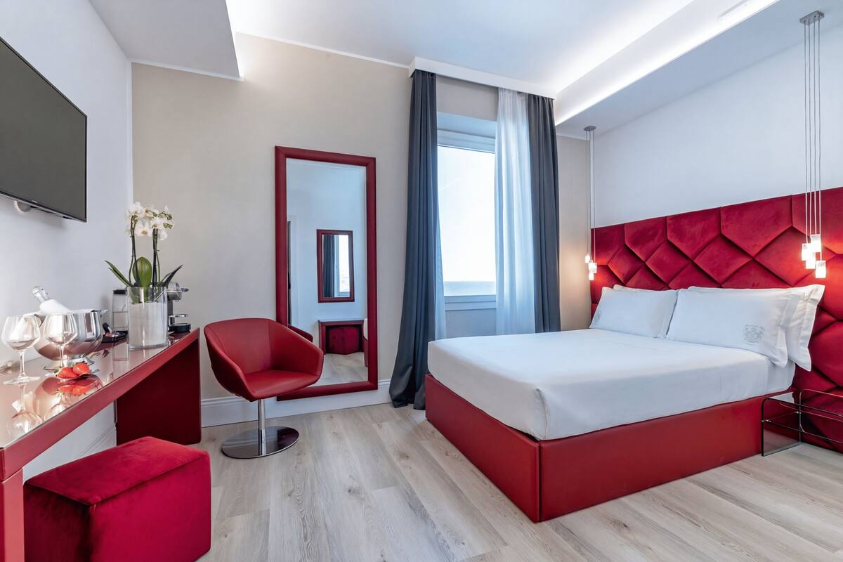 A modern hotel room with a large bed, a desk with a chair, a TV, and a window with curtains.