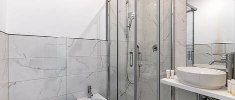 Un baño moderno con ducha de vidrio, un bidé y un lavabo con artículos de aseo.
