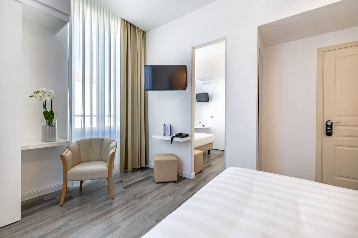 A hotel room with a bed, a chair, a desk, a TV, and a bathroom.