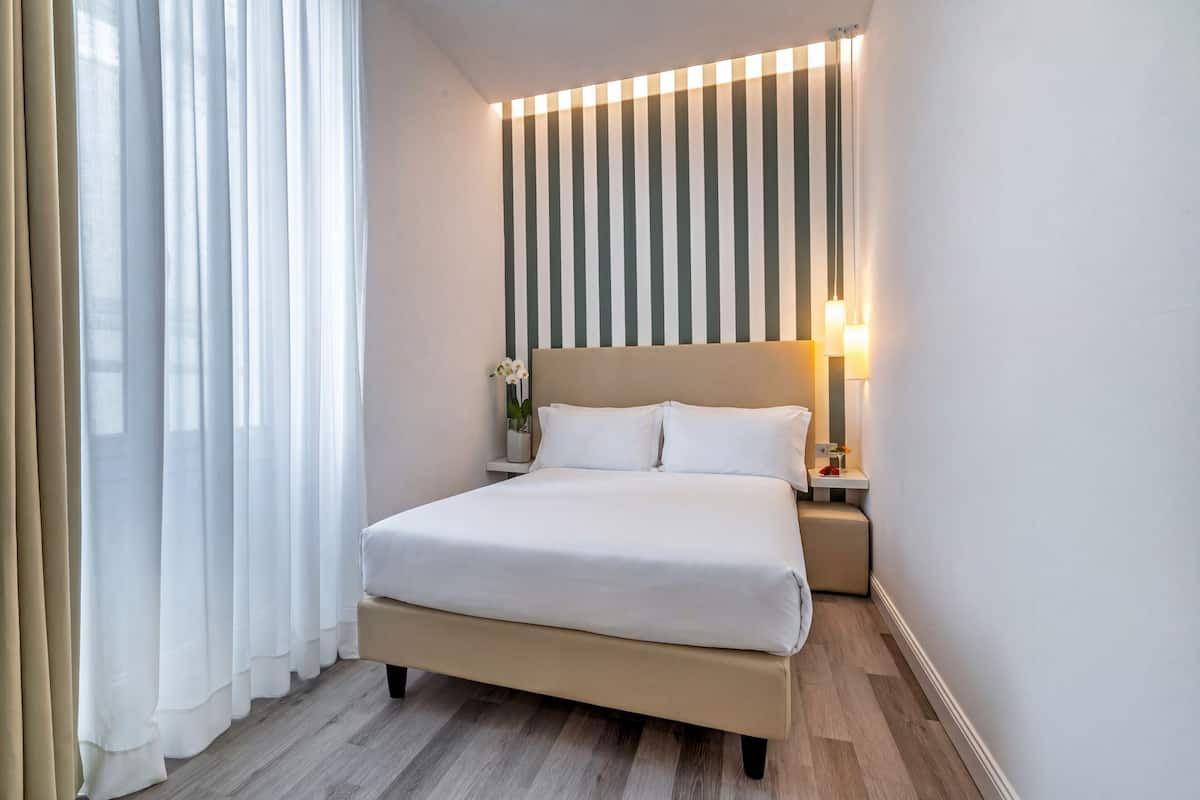 A hotel room with a bed, bedside table, lamp, and curtains.