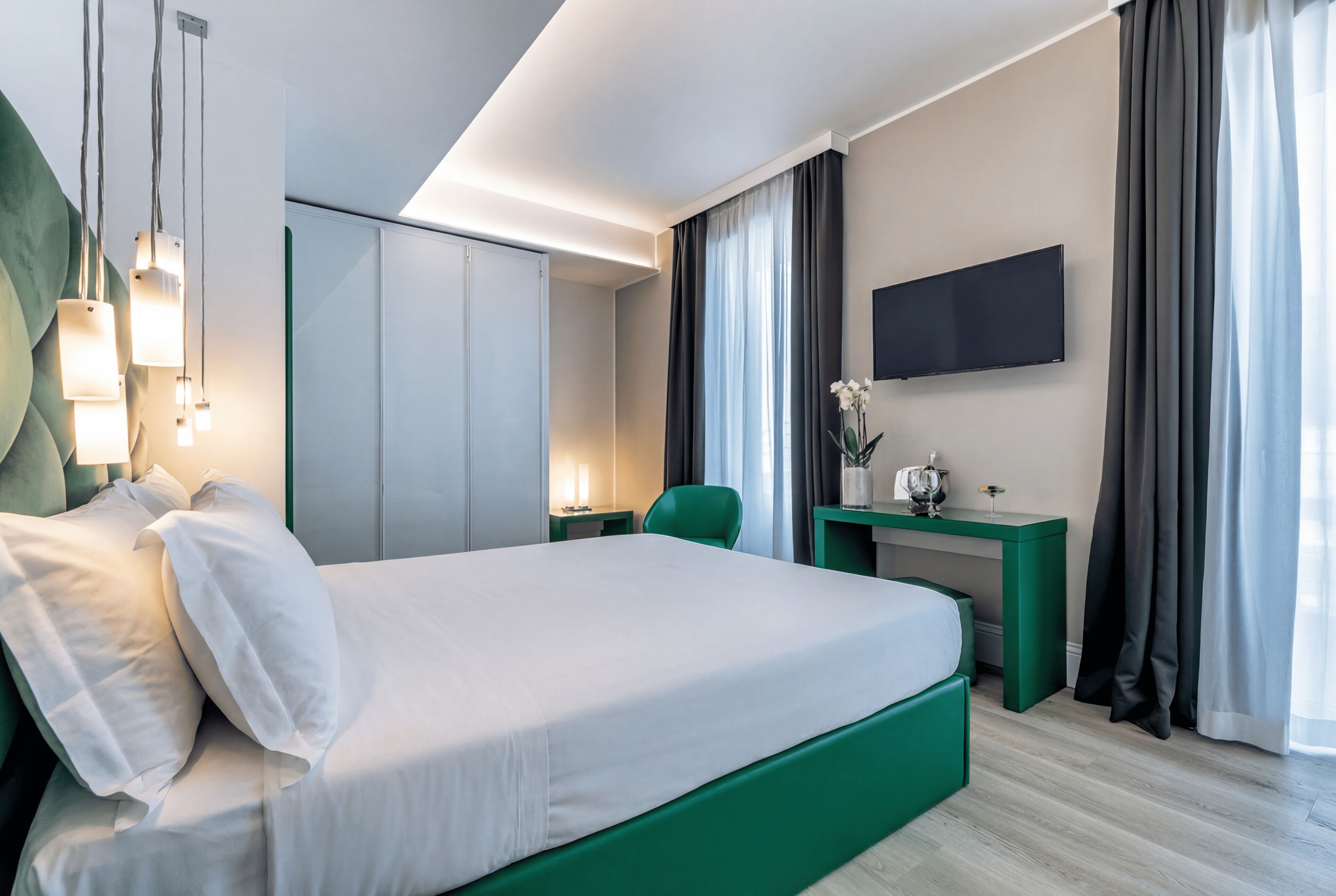 Una habitación de hotel moderna con una cama grande, un escritorio, un televisor de pantalla plana y una pared de acento verde.