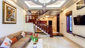 A spacious living area with a modern staircase, a flat-screen TV mounted on the wall, and a chandelier. - Gia Phat Homestay  (Da Nang)
