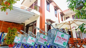 A row of bicycles with baskets labeled "Cia Dhat" parked outside a building with a balcony and outdoor seating area. - Gia Phat Homestay  (Da Nang)