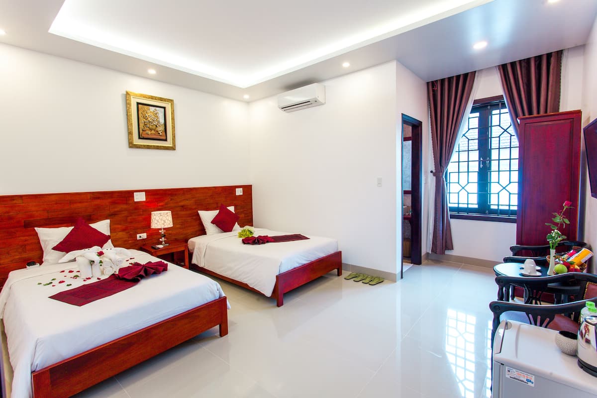 A hotel room with two beds, a dining area, and a view of the outside through a window.