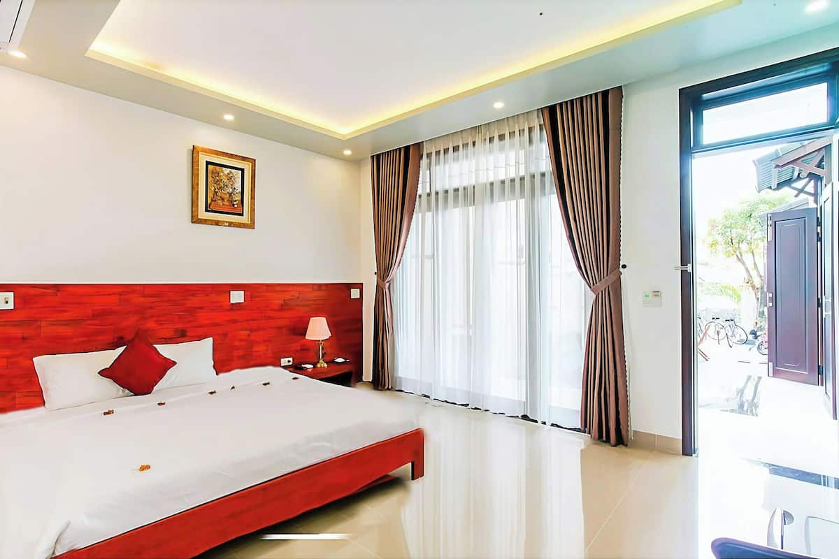 A modern hotel room with a large bed, a wooden headboard, a nightstand with a lamp, and a large window with curtains.