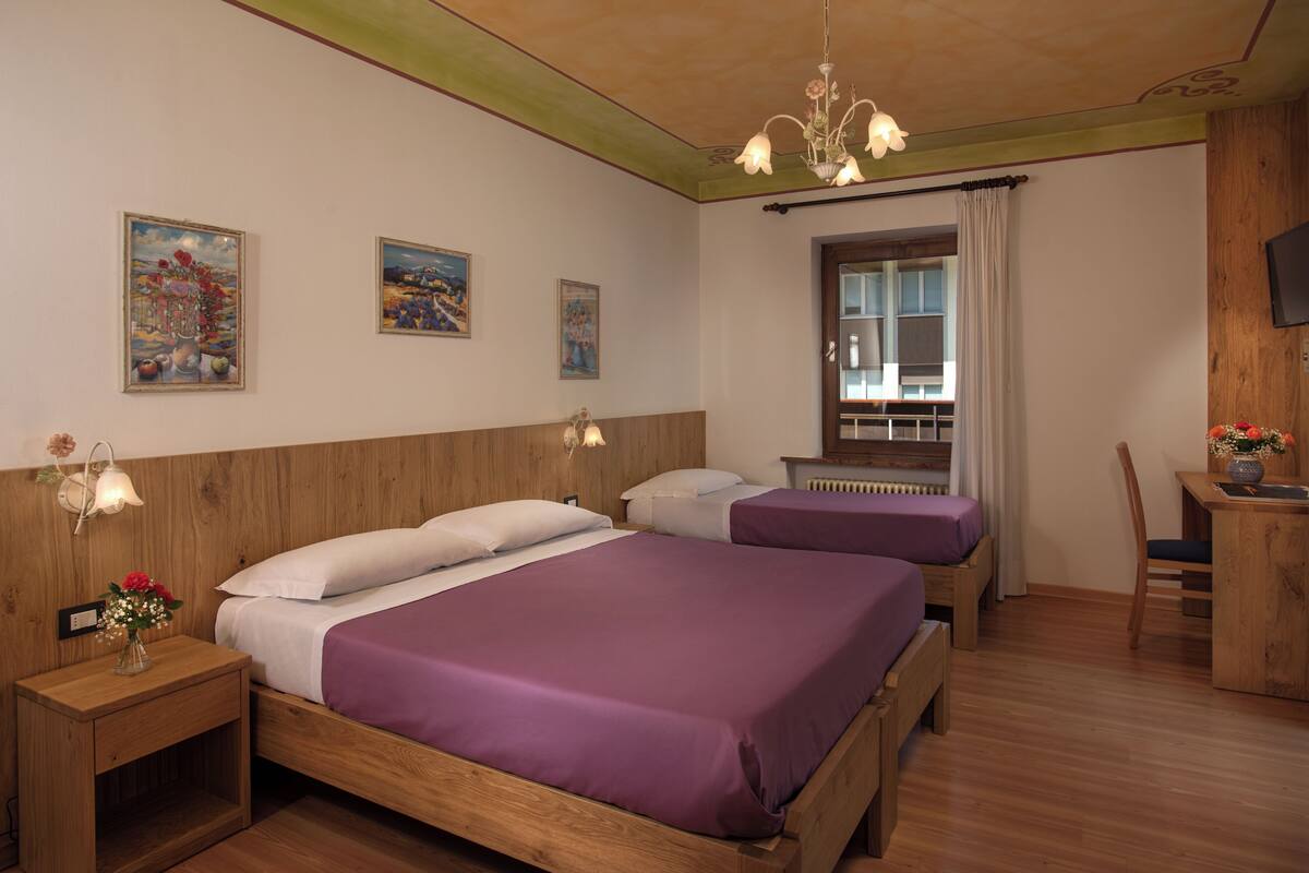 A hotel room with two beds, wooden headboards, a wooden desk, a chair, and a window with curtains.