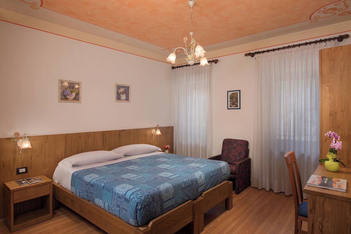 A bedroom with a wooden bed, a nightstand, a chair, a desk with a vase of flowers, and a chandelier.