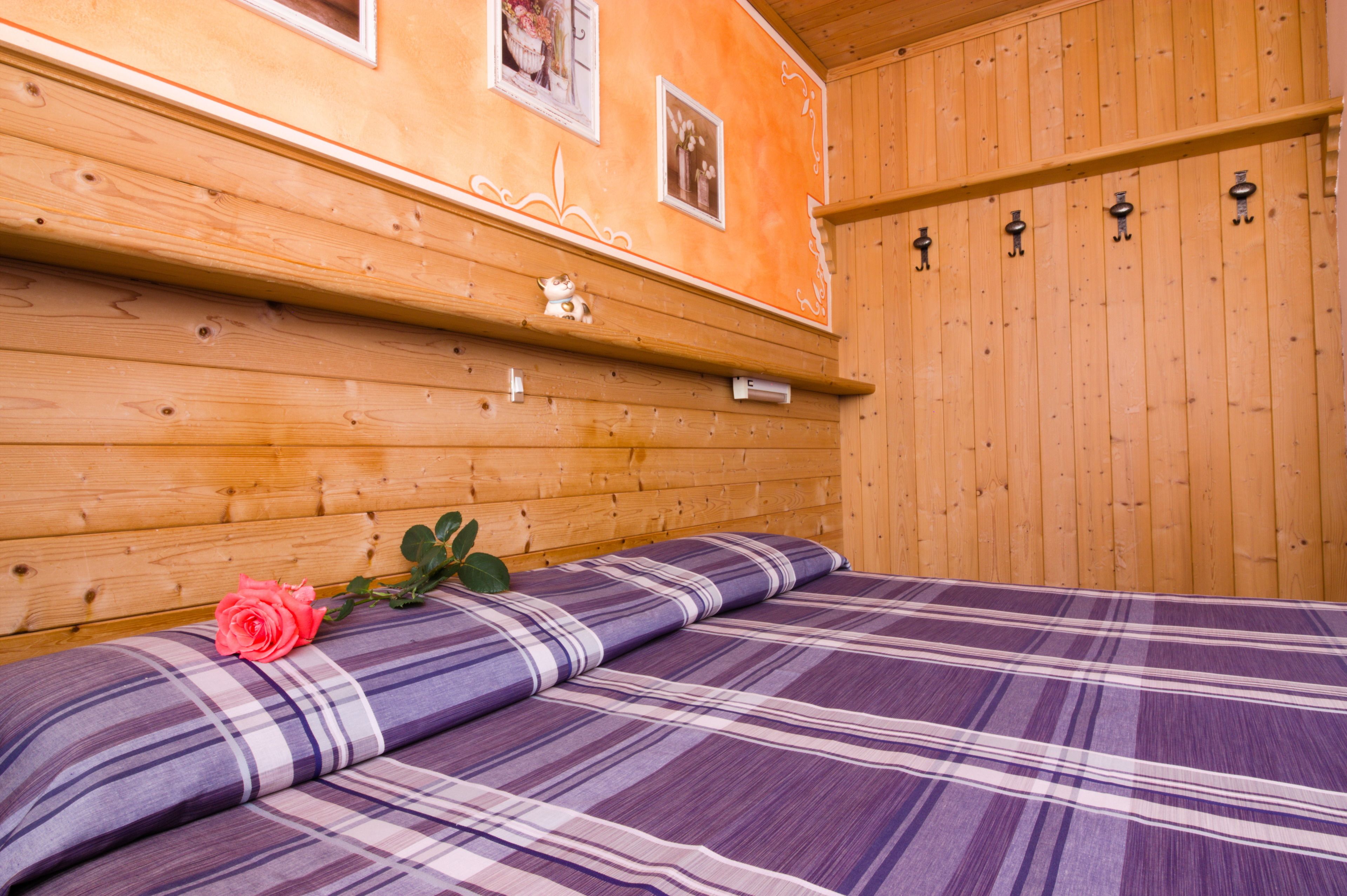 A wooden-paneled room with a bed, a shelf with a decorative item, and a wall-mounted coat rack.