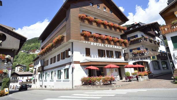 Un hotel de varios pisos con balcones decorados con flores, asientos al aire libre y vistas despejadas del entorno.