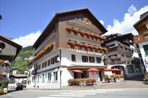 A multi-story hotel with balconies adorned with flowers, outdoor seating, and a clear view of the surrounding area. - Hotel Centrale (Alleghe)
