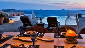 An outdoor dining area with a view of the sea, equipped with tables, chairs, and a candle centerpiece. - Villa Sunshine (Mykonos)