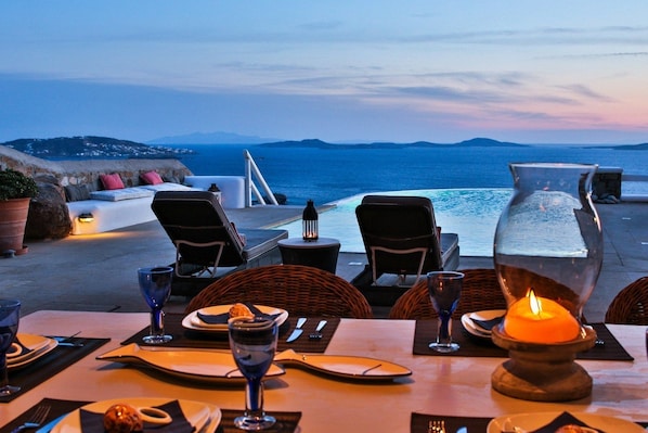 An outdoor dining area with a view of the sea, equipped with tables, chairs, and a candle centerpiece.