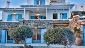 A two-story building with stone walls, blue shutters, and a balcony. - Villa Sunshine (Mykonos)