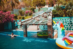A swimming pool with a person in the water, a slide, and colorful inflatable toys.