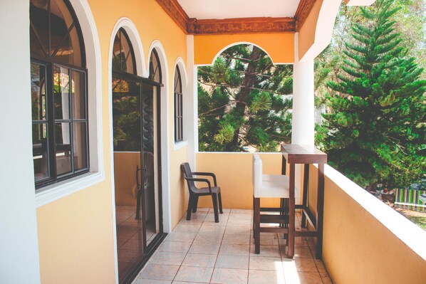 A balcony with a table and chairs, a view of trees, and a tiled floor.