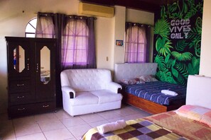 Un dormitorio con cama, un sillón blanco, un armario de madera y una pared con un mural de plantas tropicales.
