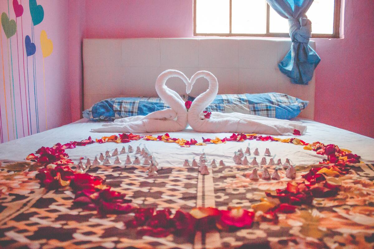 Un lit décoré avec des serviettes pliées en forme de cœur et des pétales de rose.