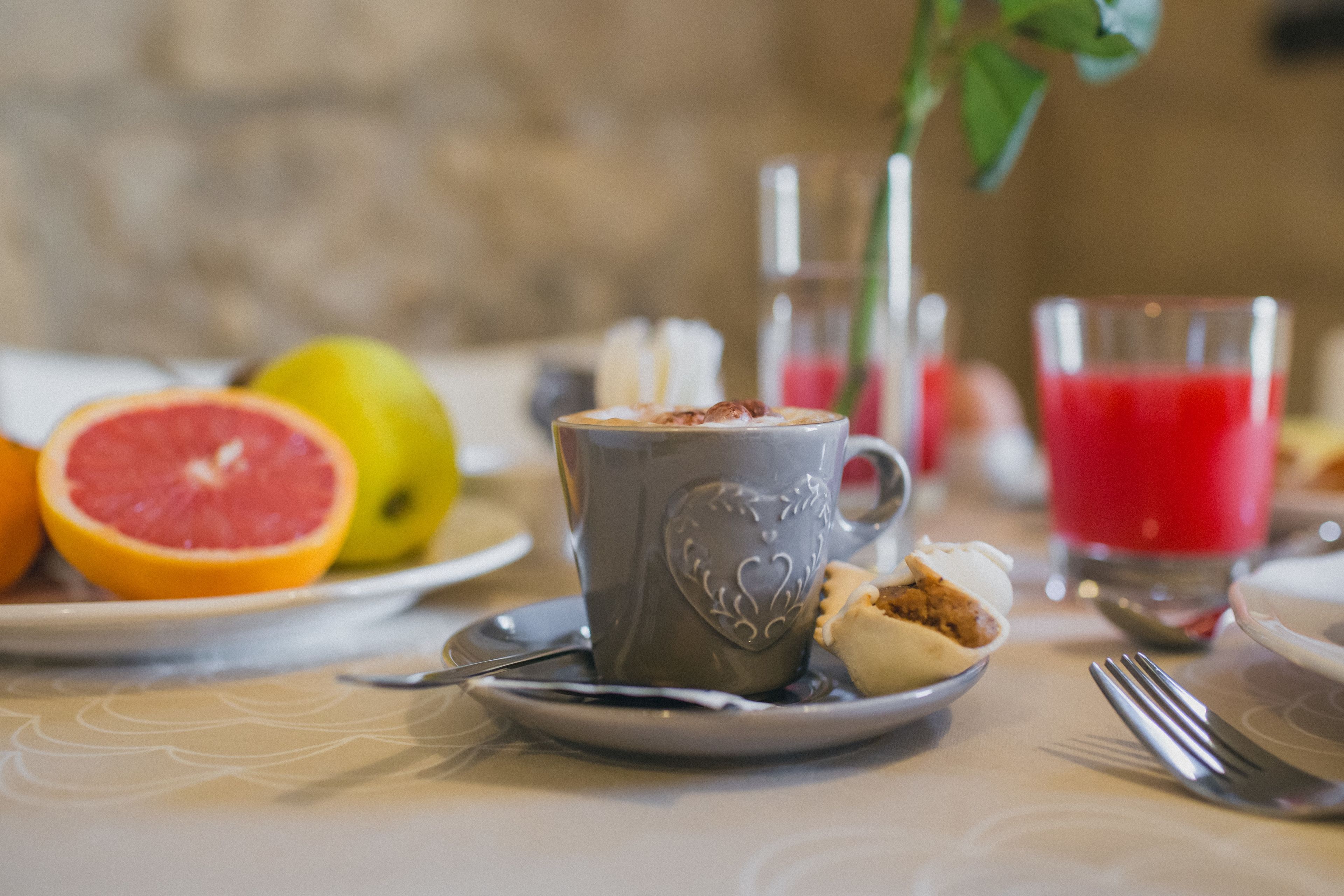 Uma mesa com uma caneca cinza, um prato com meia toranja, um copo de suco vermelho e um garfo.