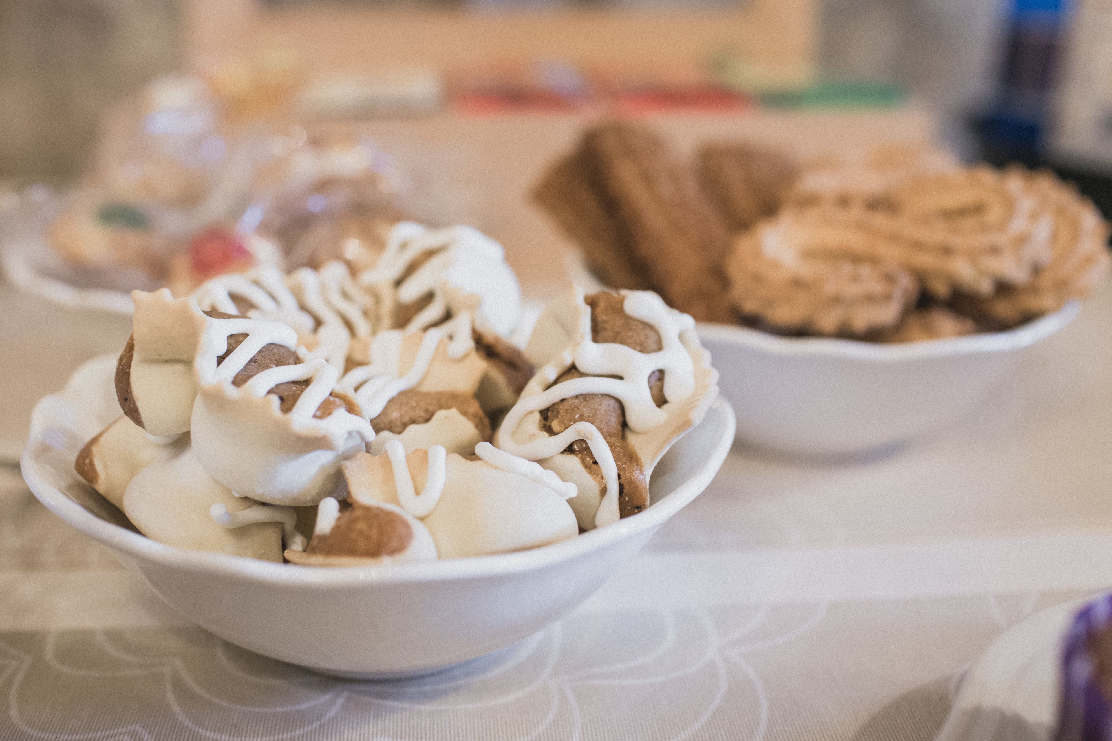 Un bol de postre con glaseado blanco y trozos marrones, y un plato de galletas al fondo.