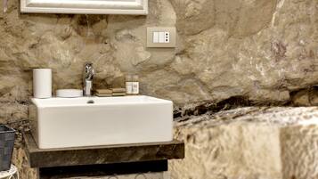 Un baño con un lavamanos blanco, un espejo y una pared de piedra.
