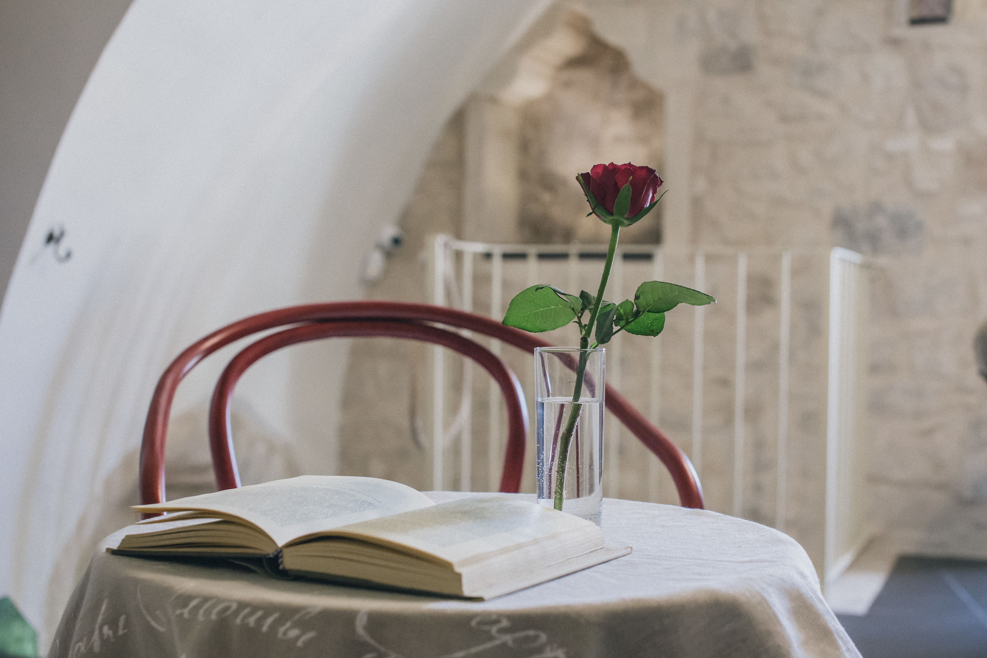 Un libro, una copa con una rosa y una silla en una habitación con paredes de piedra.