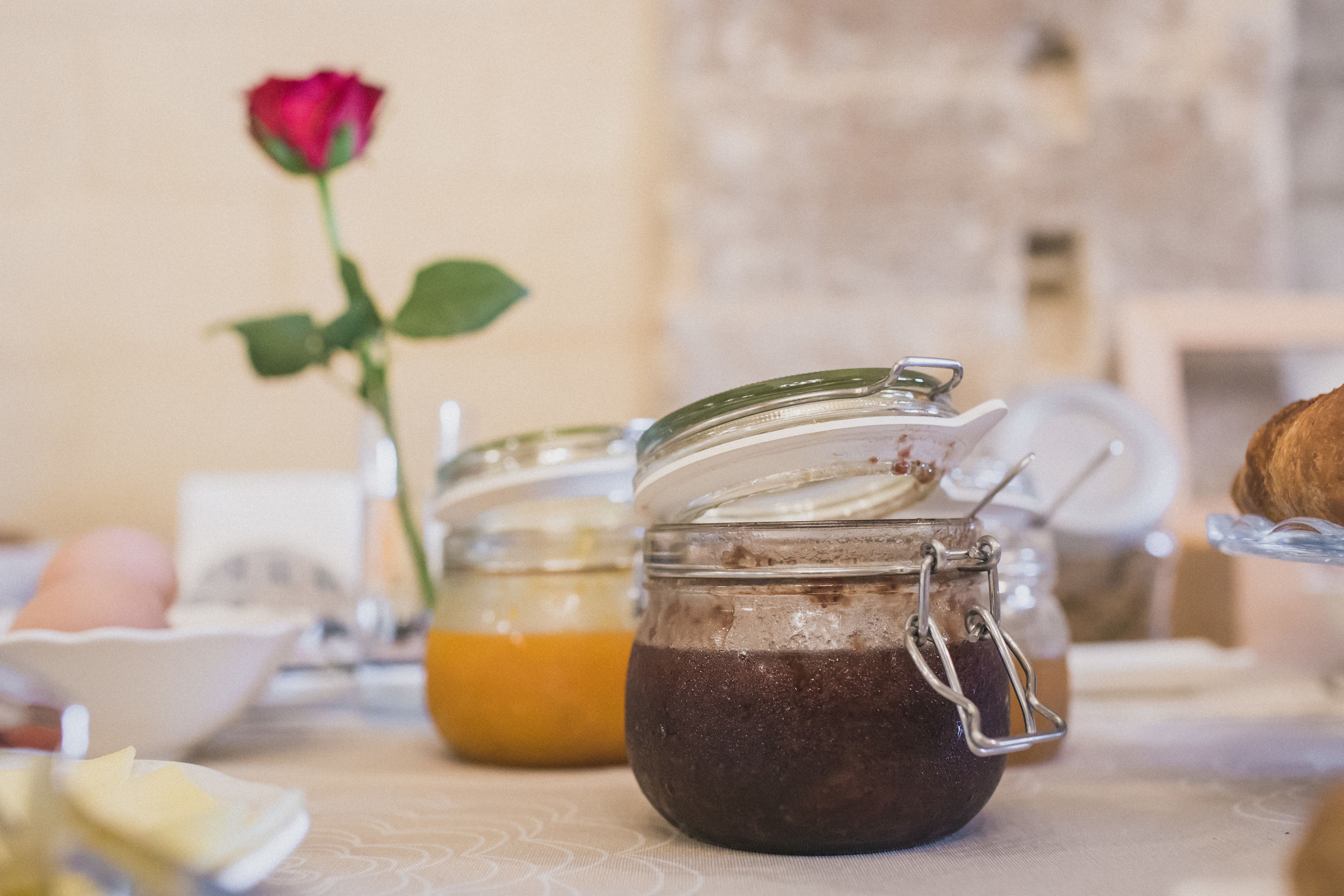 Un tavolo con due barattoli di vetro contenenti alimenti, una rosa e un piatto con una pasticceria.