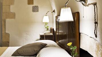 A bedroom with a bed, pillows, a bedside lamp, a nightstand, a telephone, and a wall-mounted lamp.