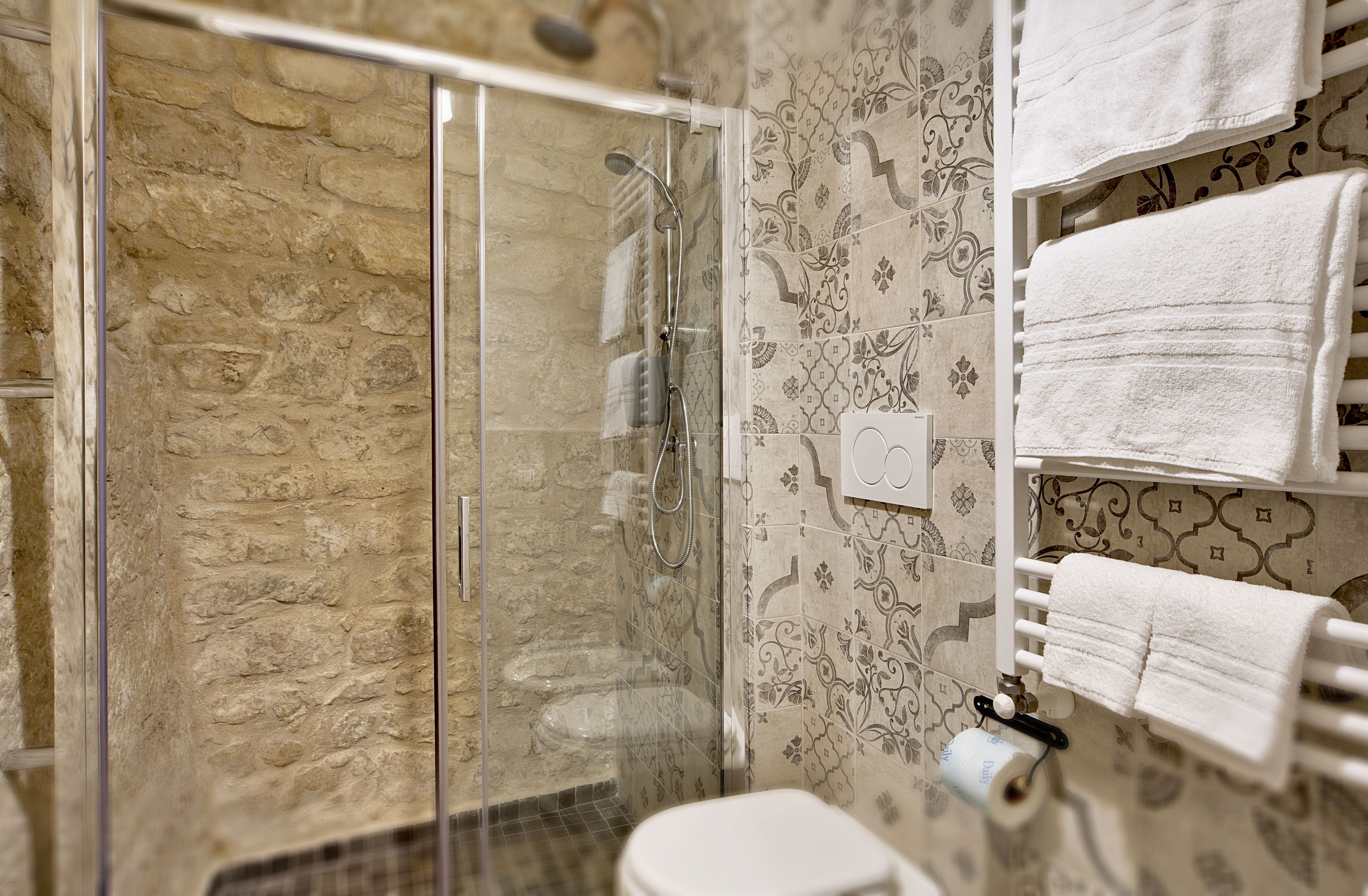 A bathroom with a glass-enclosed shower, patterned tiles, and multiple white towels on a rack.