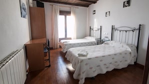 Une chambre avec deux lits, un bureau en bois, un radiateur et une fenêtre avec des rideaux.