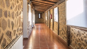 Un couloir aux murs de pierre, au plafond orné de poutres en bois et au sol carrelé.