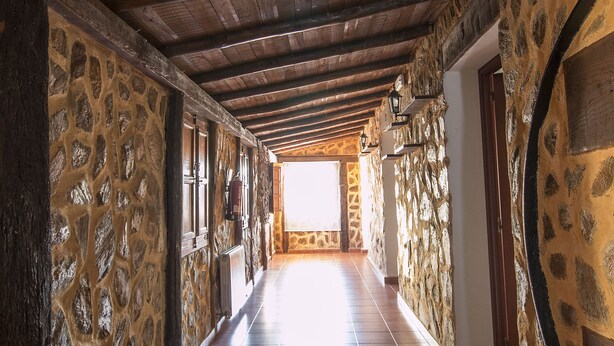 Un couloir aux murs de pierre et aux poutres en bois, qui mène à une pièce lumineuse.