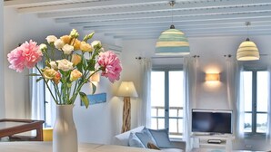 Uma sala de estar moderna com uma janela ampla, uma TV de tela plana e um vaso de flores sobre uma mesa de madeira.